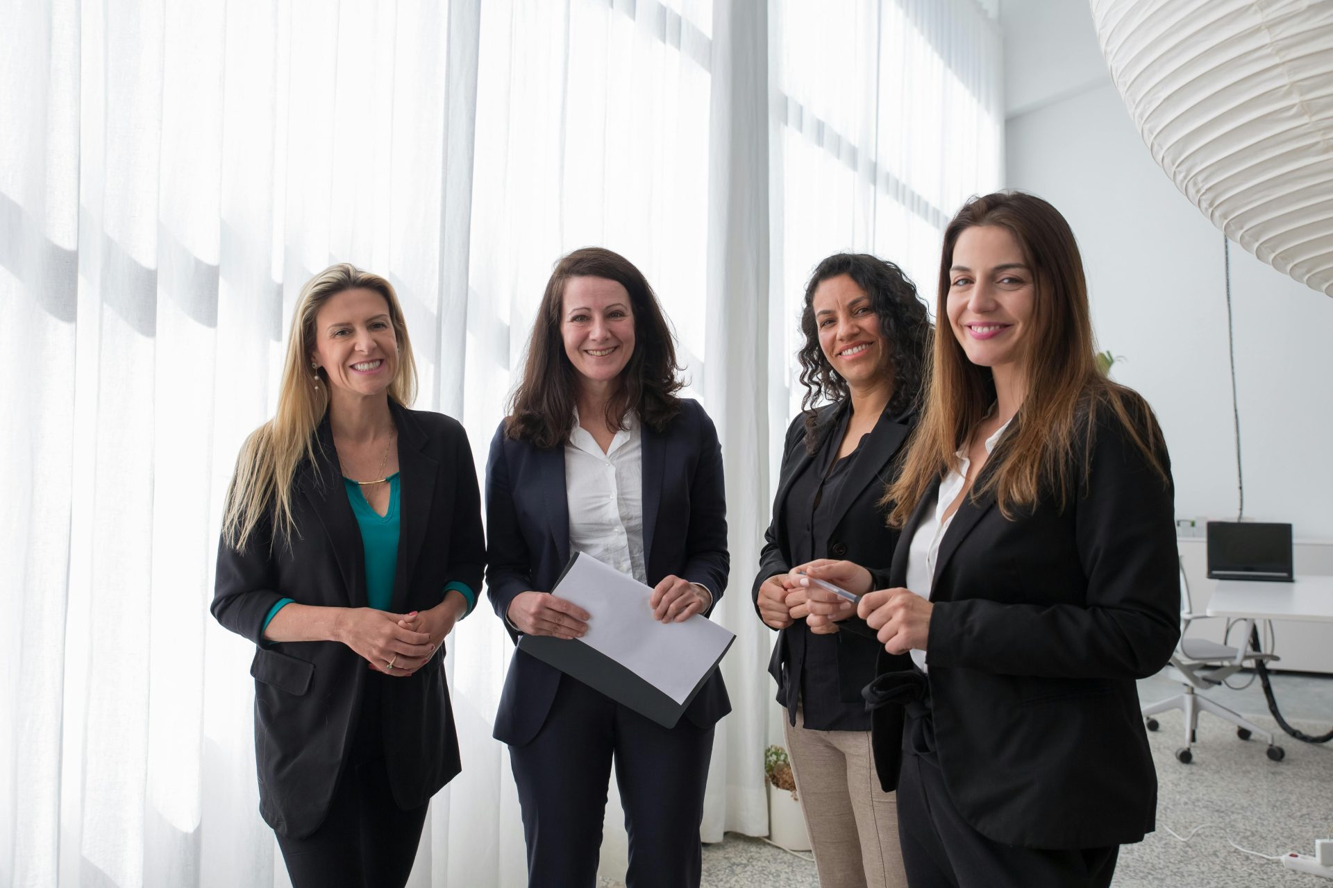 Four women in business attire smiling together